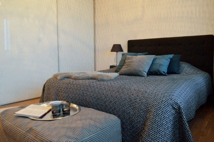 Kuvassa asunnon makuuhuone, joka on sisutettu harmailla ja mustilla tekstiileillä.